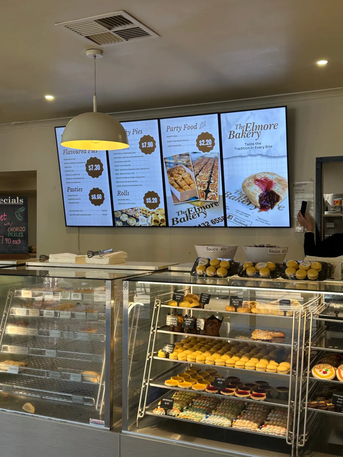 Digital menu boards above the display cabinets at Elmore Bakery